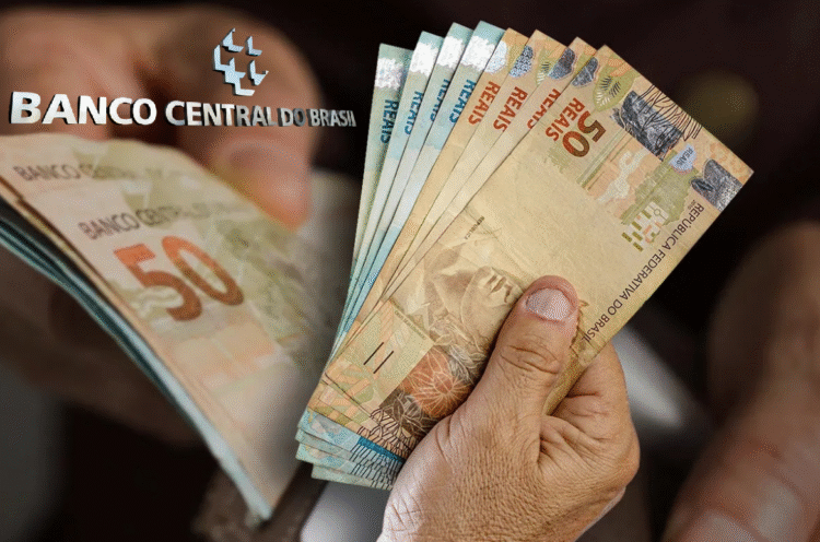 Pessoa segurando notas de reais com o logotipo do Banco Central do Brasil ao fundo.