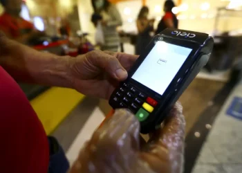 Mãos usando máquina de cartão Cielo para realizar pagamento em ambiente interno