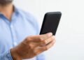 Homem de camisa social azul segurando um smartphone para consultar o comprovante de inscrição do PIS (Programa de Integração Social) pela internet.