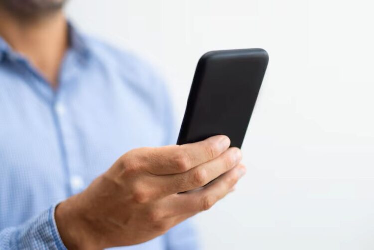 Homem de camisa social azul segurando um smartphone para consultar o comprovante de inscrição do PIS (Programa de Integração Social) pela internet.