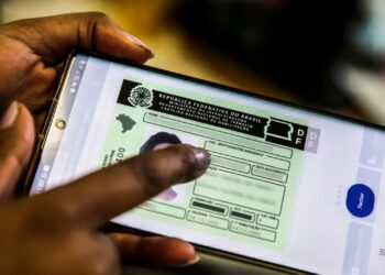 Mãos segurando um celular com a CNH digital na tela, ilustrando um artigo sobre as novas regras para recém-habilitados.