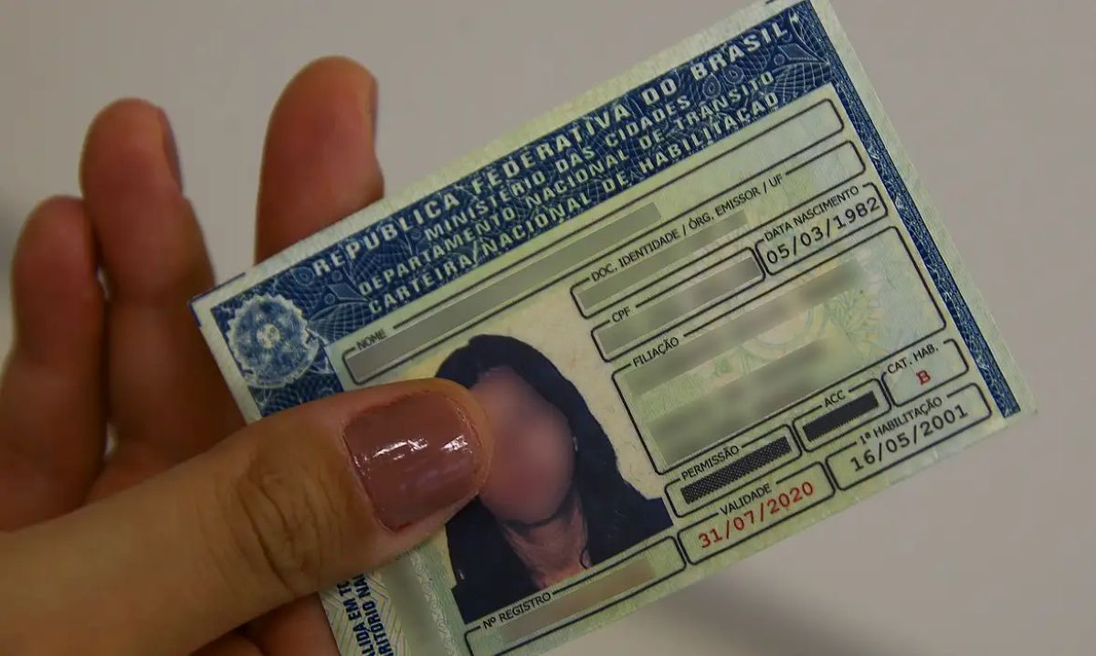 Mão feminina segurando a Carteira Nacional de Habilitação (CNH) brasileira, um símbolo do documento essencial para quem completa o processo simplificado de habilitação sem a obrigatoriedade da autoescola.