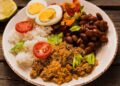 Imagem de um prato com arroz, feijão, farofa, ovos cozidos cortados ao meio e salada, representando a segurança alimentar proporcionada pelo auxílio mensal de R$ 200,00.