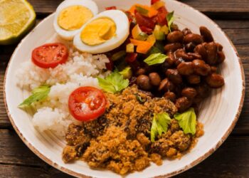 Imagem de um prato com arroz, feijão, farofa, ovos cozidos cortados ao meio e salada, representando a segurança alimentar proporcionada pelo auxílio mensal de R$ 200,00.