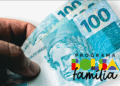 Dinheiro em notas de cem reais na mão com logo do Programa Bolsa Família.