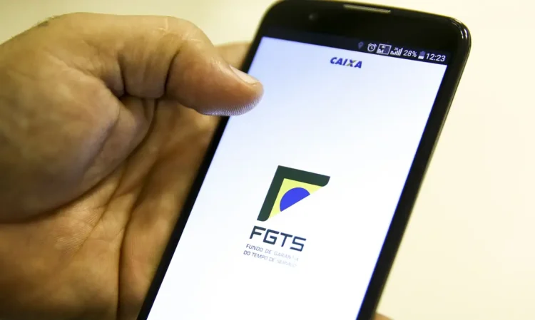 Imagem de uma mão segurando um celular e na tela está escrito FGTS