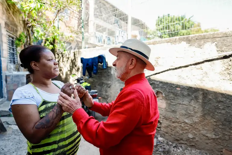 Homem idoso de chapéu e mulher sorridente dançando juntos em área externa de favela