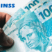 INSS divulga calendário de outubro: pagamentos começam dia 27; veja as datas 11 Mão segurando notas de 100 reais com logo do INSS ao fundo.
