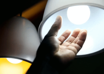 Mão estendida próxima a uma lâmpada acesa, simbolizando acesso à energia elétrica.