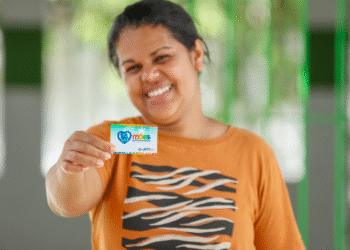 Mulher sorrindo segura o cartão do programa Mães de Pernambuco.