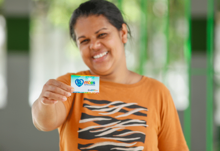 Mulher sorrindo segura o cartão do programa Mães de Pernambuco.
