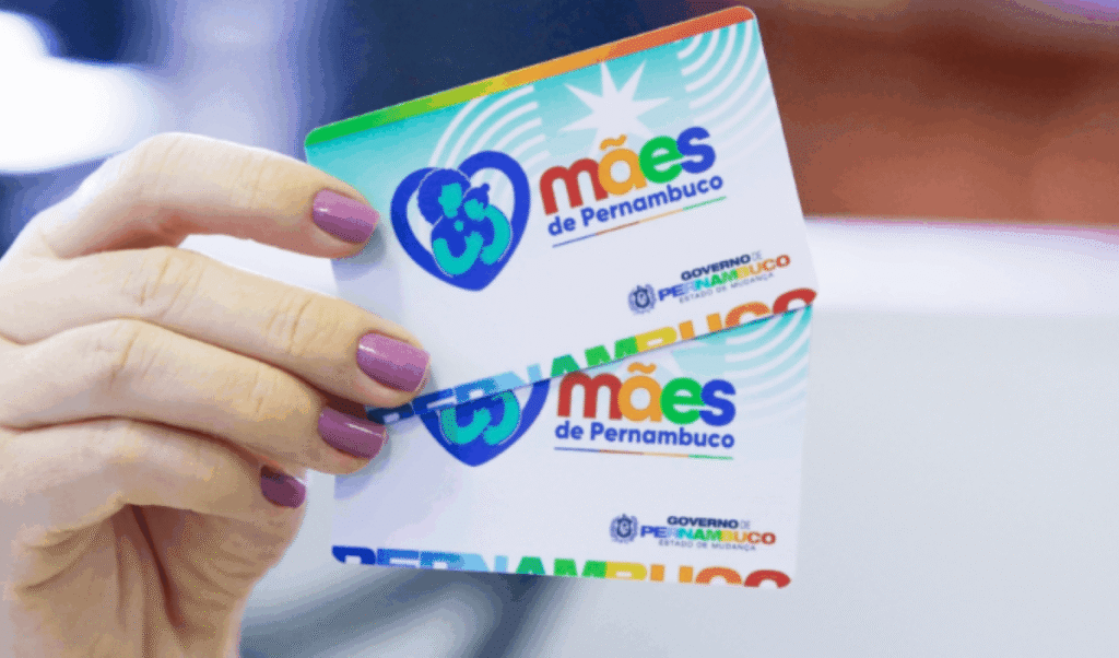 Mão segurando cartões coloridos com logo do Programa Mães de Pernambuco sobre pagamento de parcela.