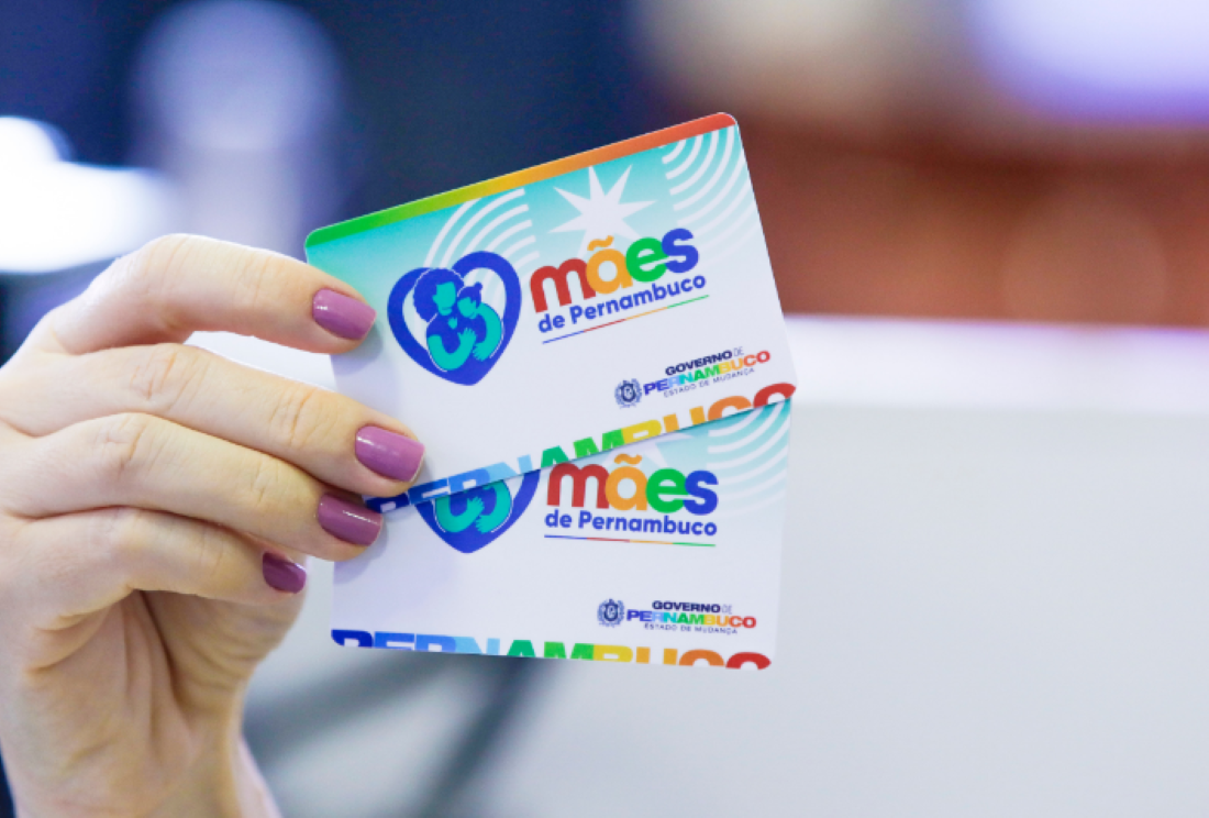 Cartões do programa Mães de Pernambuco segurados por uma mão.