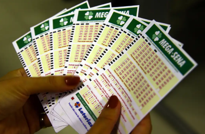 Pessoa segurando vários volantes da Mega-Sena com números marcados.