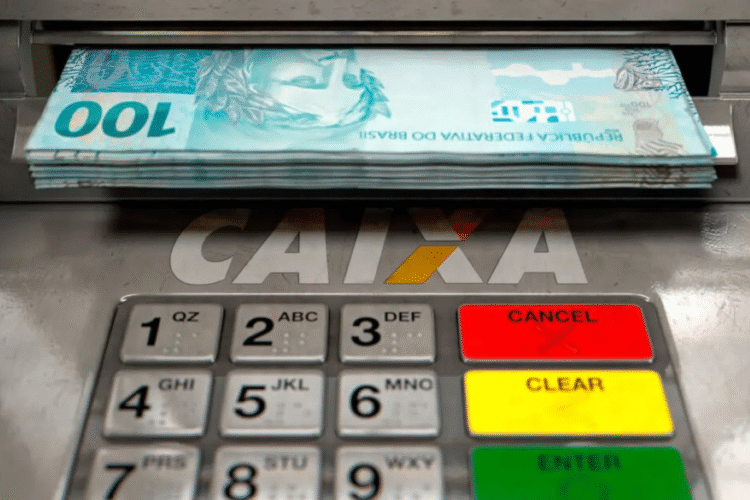 Notas de dinheiro sendo dispensadas por caixa eletrônico da CAIXA.