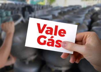 Mão segurando um cartão com o texto “Vale Gás” em frente a botijões de gás desfocados.