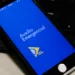 ATENÇÃO: Governo reabre prazo para devolver Auxílio Emergencial recebido indevidamente 11 Tela de smartphone mostrando o aplicativo Auxílio Emergencial aberto em fundo azul com símbolo amarelo