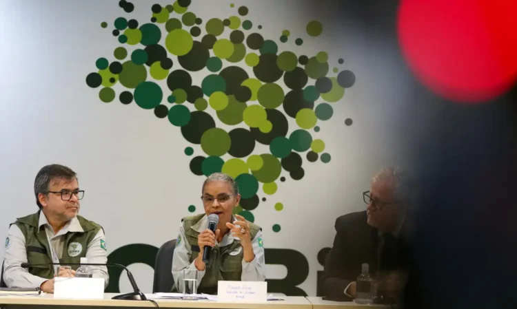 Pessoas em reunião formal do ICMBio com microfone e mural de círculos verdes ao fundo