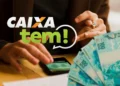 Mãos sobre celular com logo da Caixa e a frase "Caixa Tem!", ao lado de notas de 100 reais, ilustrando o Pix premiado.