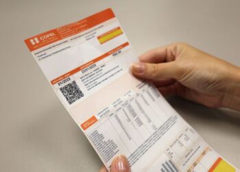 Mãos segurando uma conta de luz com informações de consumo e bandeira tarifária, representando a economia na energia.