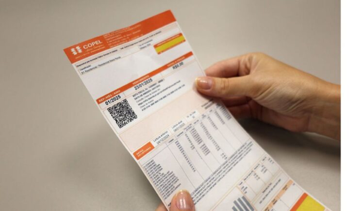 Mãos segurando uma conta de luz com informações de consumo e bandeira tarifária, representando a economia na energia.