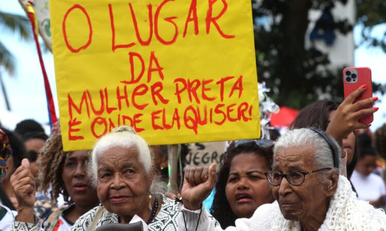 Marcha Nacional das Mulheres Negras do Bolsa Família acontece dia 25 de novembro 1 Pessoas em protesto segurando placa amarela com frase sobre lugar da mulher preta