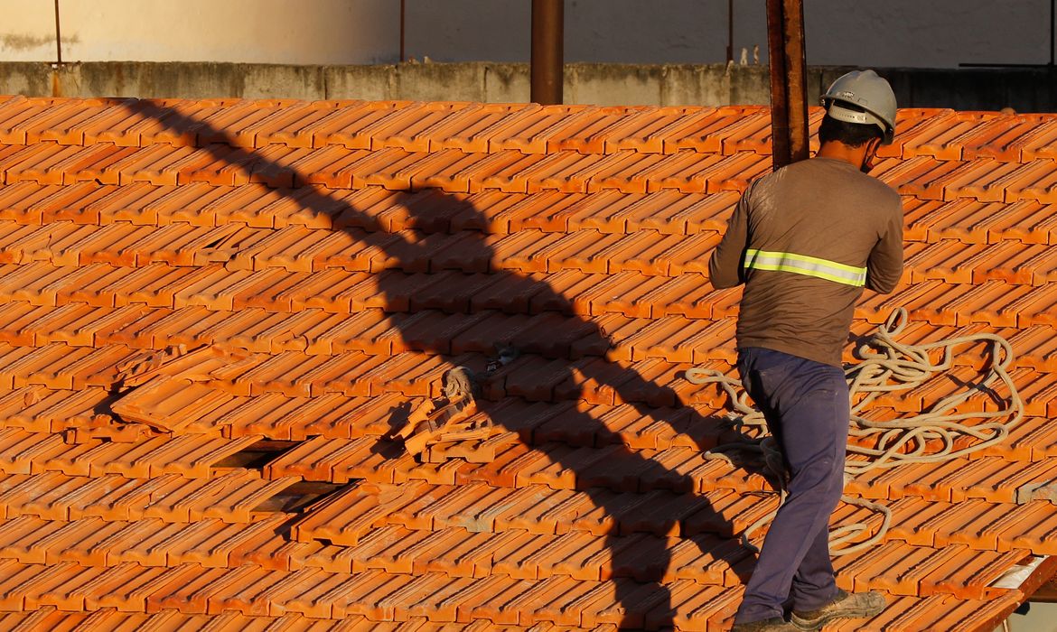 Trabalhador de segurança em telhado de cerâmica Homem com capacete e roupa de segurança trabalhando em telhado de cerâmica laranja sob luz do sol