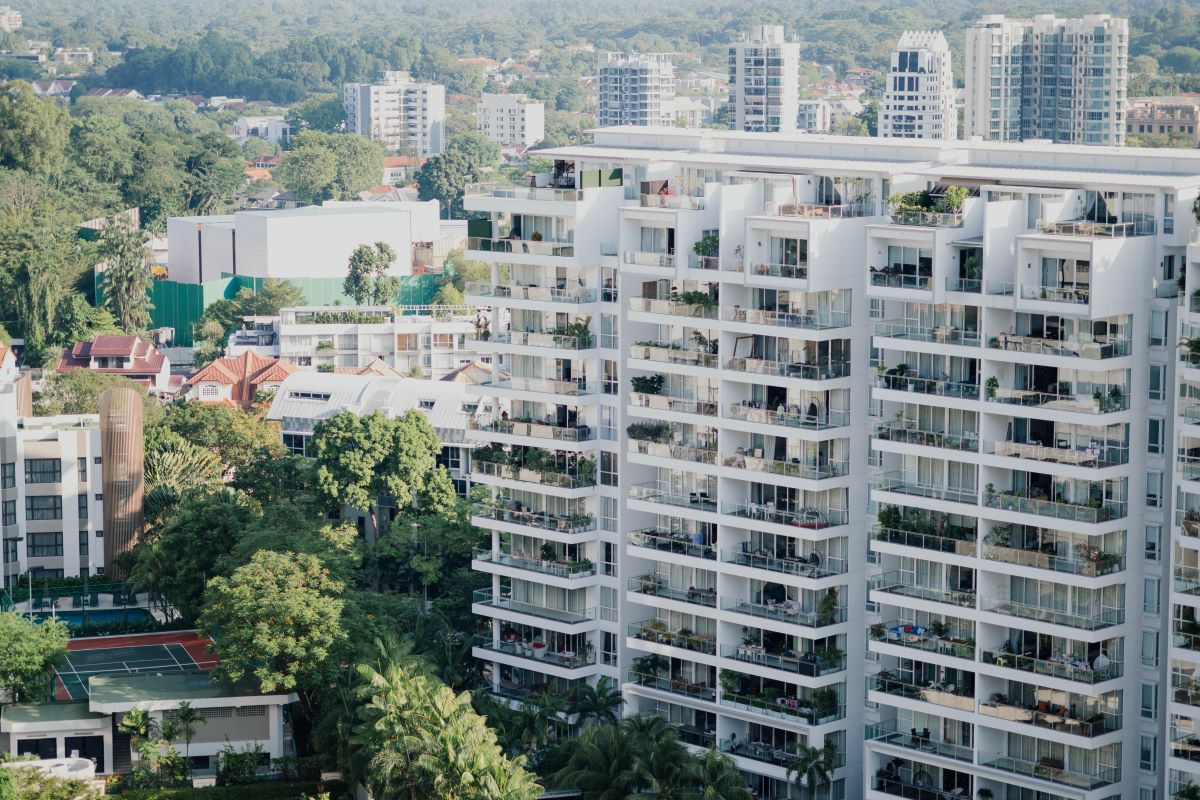 Vista aérea de prédio residencial moderno com varandas amplas, áreas verdes e quadra esportiva em condomínio