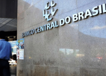 Fachada do edifício do Banco Central do Brasil com letreiro "Banco Central do Brasil" e pessoa caminhando em frente.