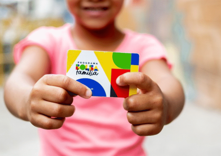Criança segurando um cartão do programa Bolsa Família com as duas mãos.
