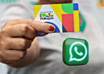 Pessoa segura um cartão do Programa Bolsa Família com o ícone do WhatsApp ao lado.