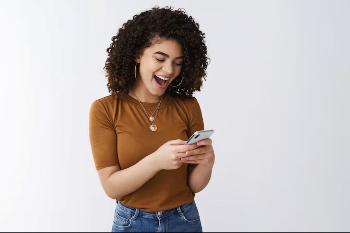 Jovem mulher feliz usando o celular para agendamento online, simbolizando a facilidade digital.