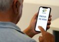 Homem idoso usando smartphone com o aplicativo "Meu INSS" exibindo "PROVA DE VIDA".
