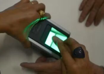 Pessoa realizando coleta de digitais em equipamento biométrico durante atendimento público.