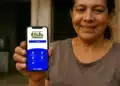 Mulher sorridente segurando celular com aplicativo do Programa Bolsa Família aberto na tela