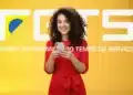 Mulher sorridente segurando celular em frente ao logotipo do FGTS em fundo amarelo, representando a consulta ao saque-aniversário.