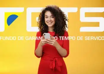 Saque aniversário FGTS: Caixa libera valores retidos na próxima segunda (29); confira 5 Mulher sorridente segurando celular em frente ao logotipo do FGTS em fundo amarelo, representando a consulta ao saque-aniversário.