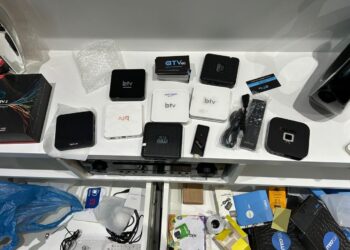 Vários modelos de TV Box, controles remotos, cabos e acessórios organizados sobre mesa branca