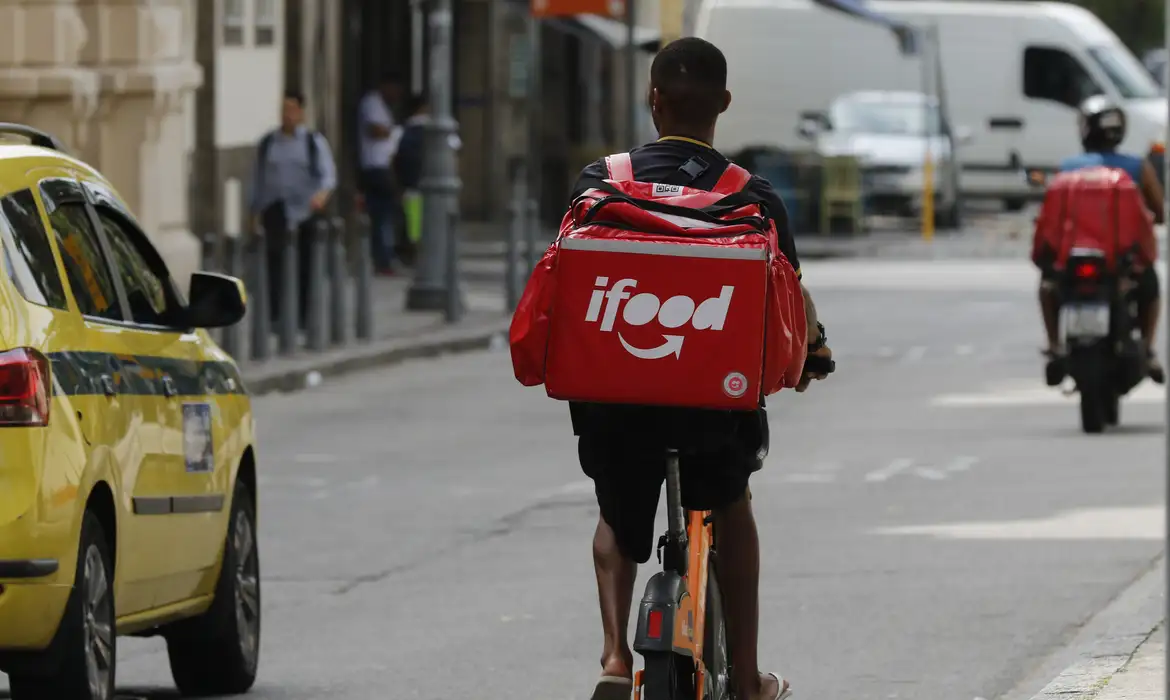 Entregador de bicicleta do iFood pedalando na rua, representando os profissionais que buscam alto desempenho para participar do programa de premiação Super.