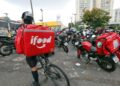 Entregador de bicicleta com mochila do iFood em uma concentração de motoboys. A imagem representa a comunidade de trabalhadores beneficiados pelo bônus de até R$ 3.000.