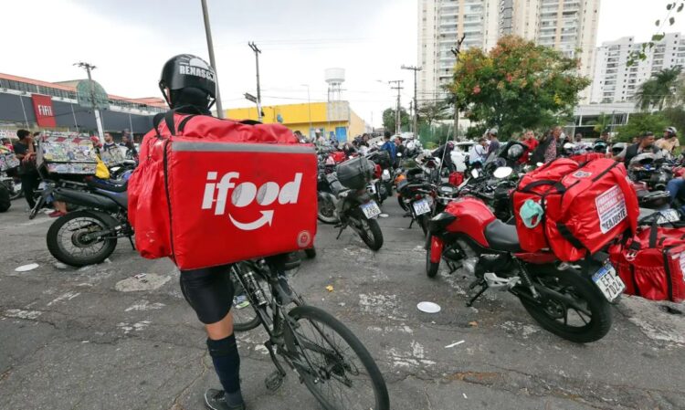 Entregador de bicicleta com mochila do iFood em uma concentração de motoboys. A imagem representa a comunidade de trabalhadores beneficiados pelo bônus de até R$ 3.000.