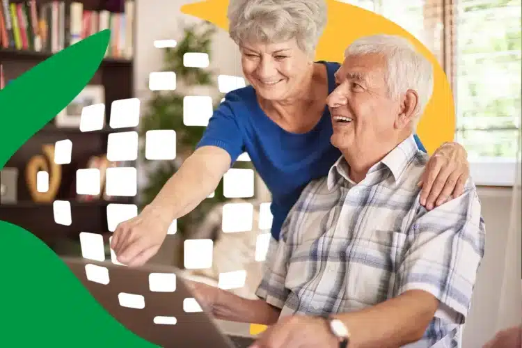 Casal de idosos sorrindo enquanto usam um laptop juntos em casa.