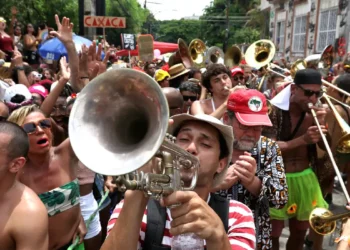 Carnaval 2026: veja os horários de atendimento dos bancos 5 Músicos com fantasias tocam trompete e trombone em meio à multidão festiva em bloco carnavalesco
