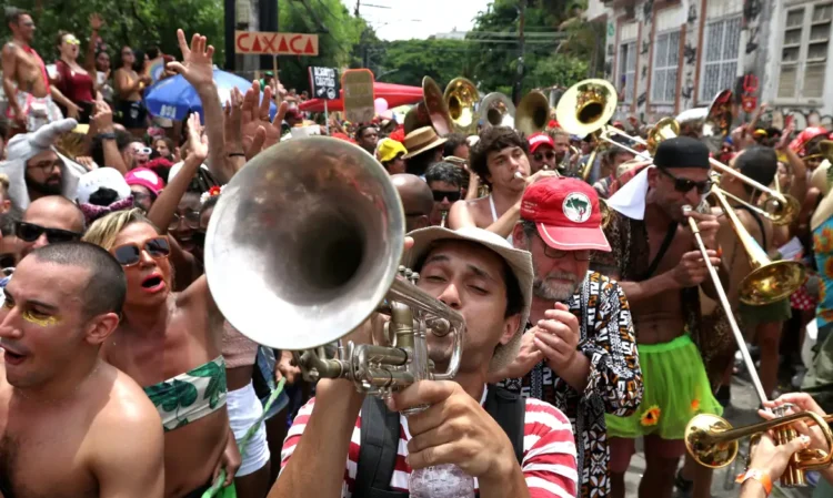Carnaval 2026: veja os horários de atendimento dos bancos 1 Músicos com fantasias tocam trompete e trombone em meio à multidão festiva em bloco carnavalesco