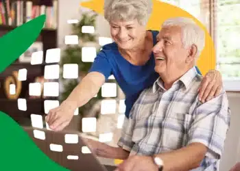 Aposentados poderão comparar ofertas e escolher a melhor taxa no novo leilão do INSS 5 Mulher sorrindo aponta para tela de notebook ao lado de homem idoso sentado na sala