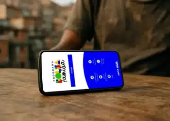 Uso de Pix ou cartão pode mesmo cancelar o Bolsa Família? 7 Celular exibindo aplicativo Bolsa Família sobre mesa de madeira em ambiente urbano desfocado